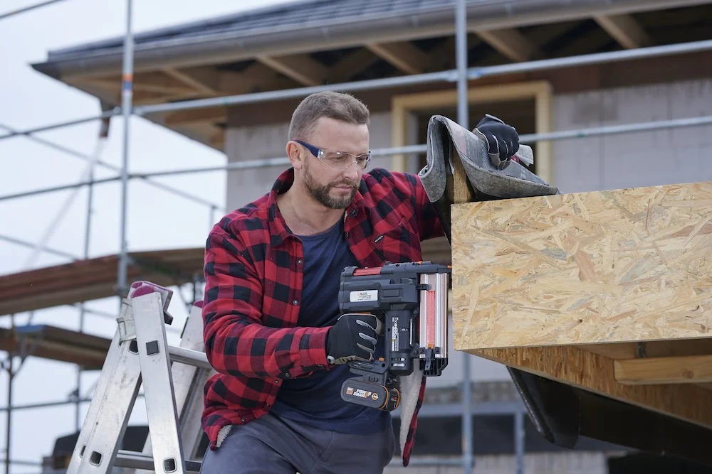 Person befestigt Holzplatte mit Druckluftnagler